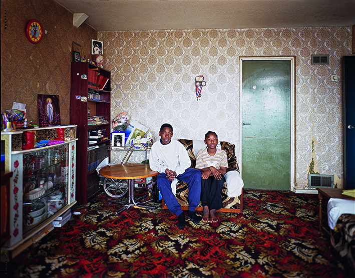 Photograph of two people sitting on a sofa in a council flat on the Holly Street estate Hackney